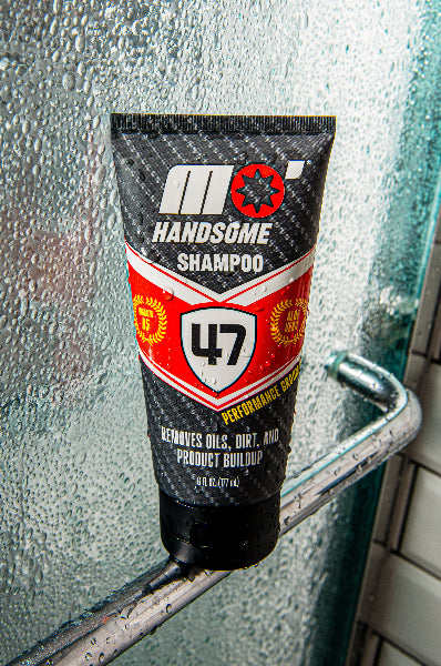 Mo’Handsome red Ferrari-inspired shampoo tube balanced on shower slide door—clean design meets high-performance style.