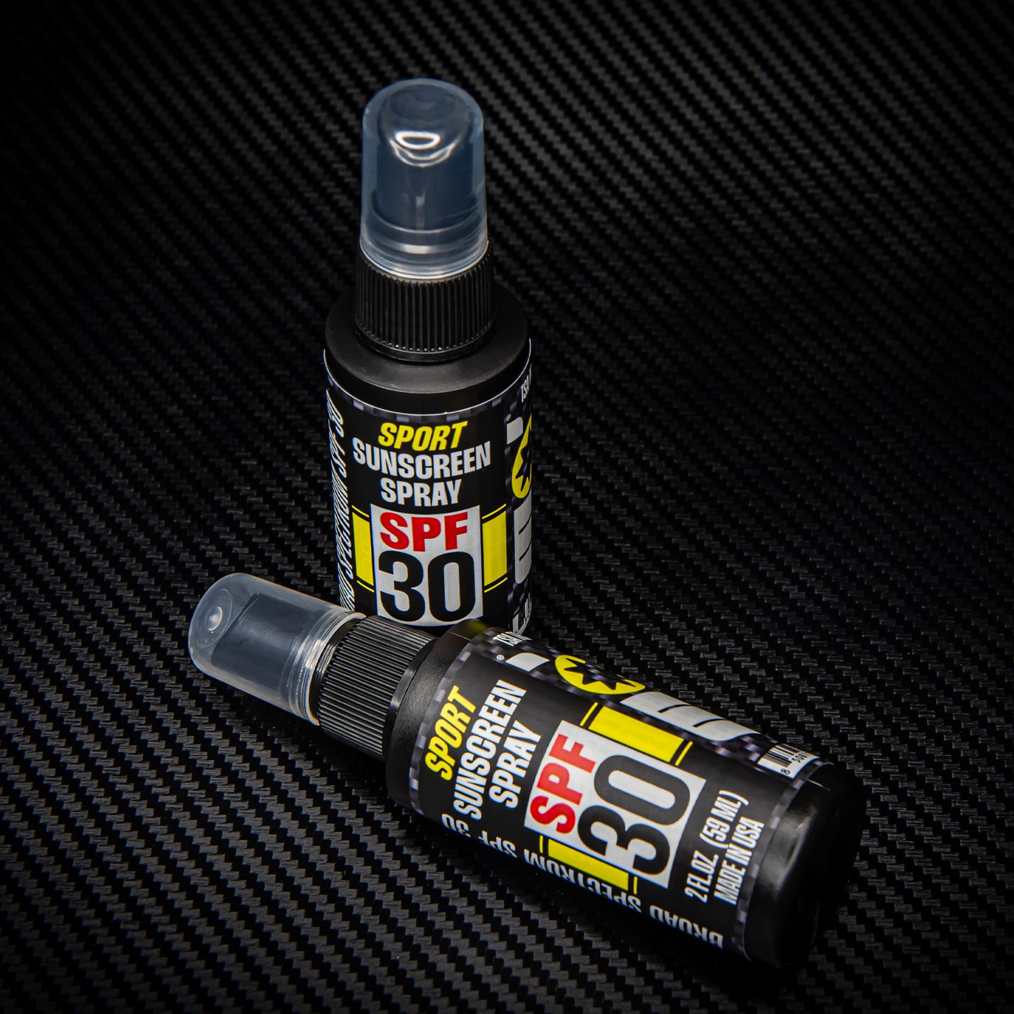 2 pack spf 30 sport sunscreen spray TSA approved standing and laying on black carbon fiber background